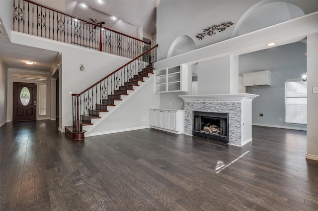 unfurnished living room with a towering ceiling, baseboards, dark wood-style flooring, a tiled fireplace, and stairs
