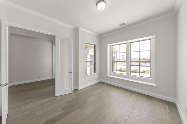 empty room with baseboards, ornamental molding, wood finished floors, and visible vents
