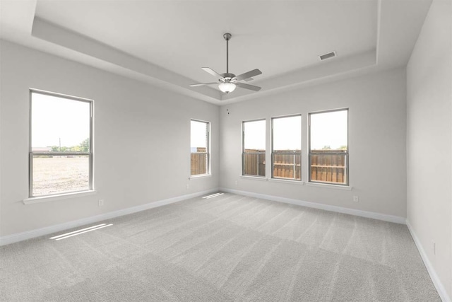 carpeted spare room with ceiling fan, baseboards, a tray ceiling, and visible vents