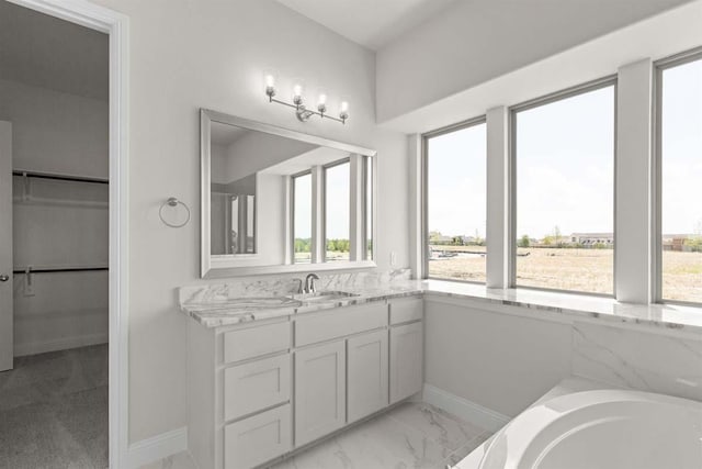bathroom featuring baseboards, vanity, a walk in closet, and a healthy amount of sunlight