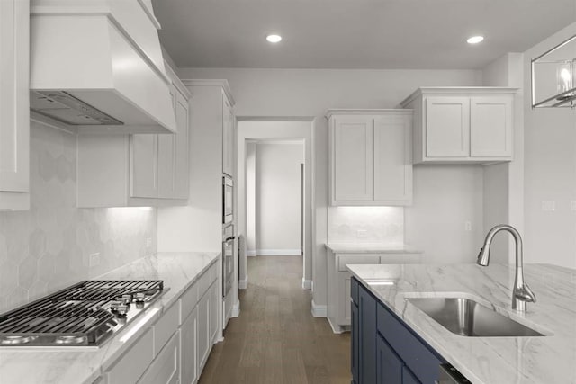 kitchen with white cabinets, custom exhaust hood, a sink, and appliances with stainless steel finishes