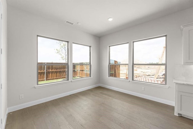 unfurnished room with baseboards, light wood-style floors, visible vents, and plenty of natural light