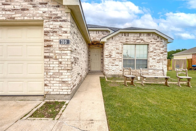 view of exterior entry with a garage, fence, a yard, and brick siding