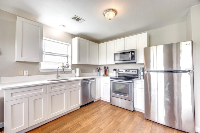 kitchen featuring white cabinets, appliances with stainless steel finishes, a sink, light countertops, and visible vents