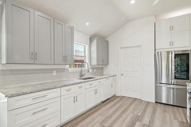 kitchen featuring a sink, smart refrigerator, vaulted ceiling, decorative backsplash, and white dishwasher