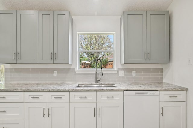 kitchen with backsplash, dishwasher, gray cabinets, a sink, and light stone countertops