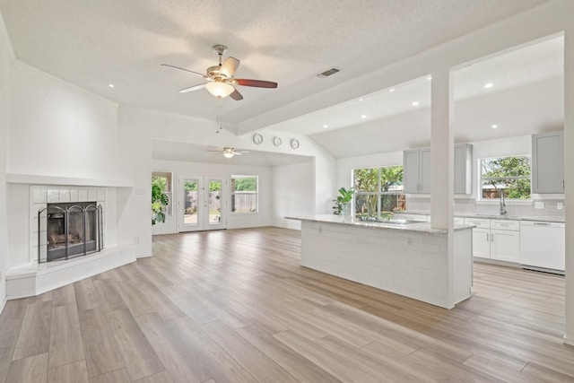 unfurnished living room featuring a ceiling fan, light wood-type flooring, a tile fireplace, lofted ceiling, and visible vents