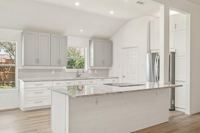 kitchen featuring a sink, light wood-type flooring, freestanding refrigerator, backsplash, and lofted ceiling