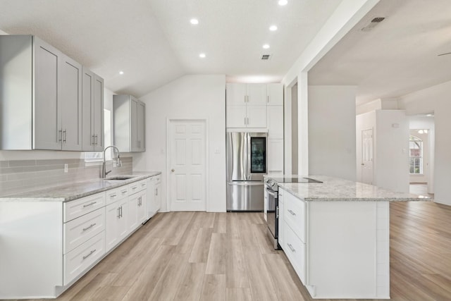 kitchen with appliances with stainless steel finishes, light stone countertops, a sink, and light wood finished floors