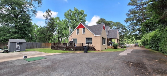 view of side of home featuring a wooden deck, fence, an outdoor structure, a storage unit, and a shingled roof