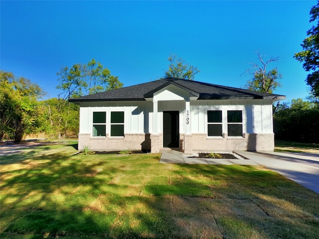 bungalow-style home featuring board and batten siding, brick siding, a front yard, and roof with shingles