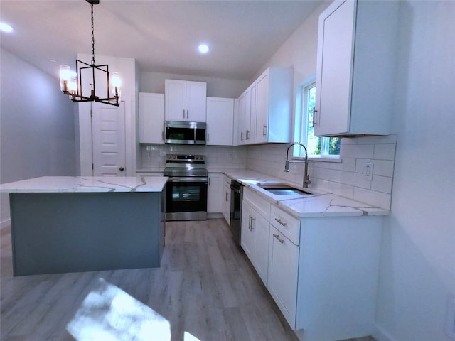 kitchen with light stone counters, stainless steel appliances, backsplash, a sink, and a notable chandelier