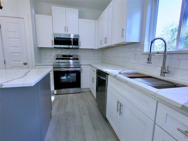 kitchen featuring a sink, light wood-style floors, stainless steel appliances, backsplash, and white cabinetry