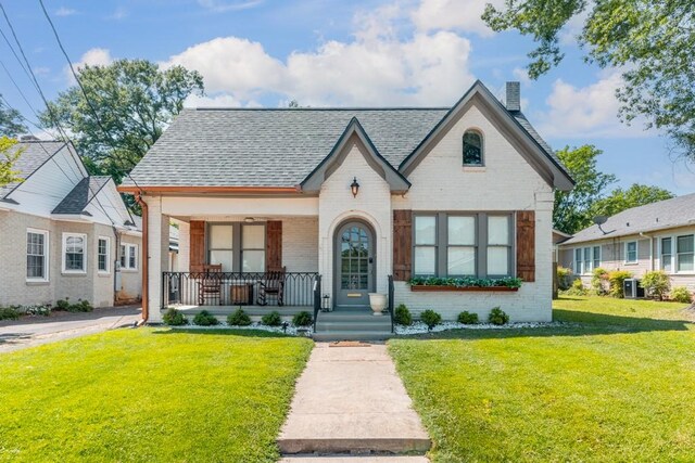 view of front of property featuring brick siding, a shingled roof, a front yard, and covered porch