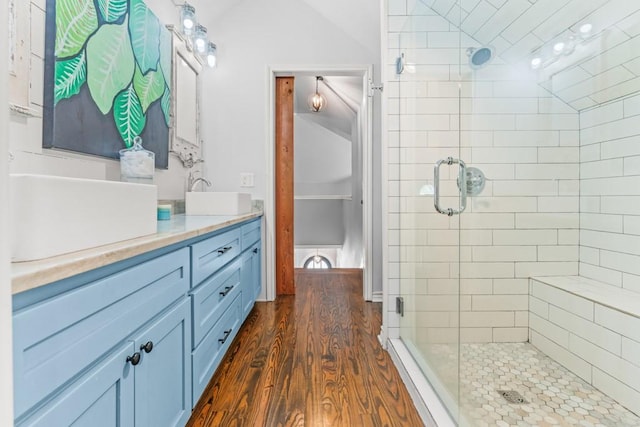 bathroom with a sink, double vanity, lofted ceiling, wood finished floors, and a shower stall