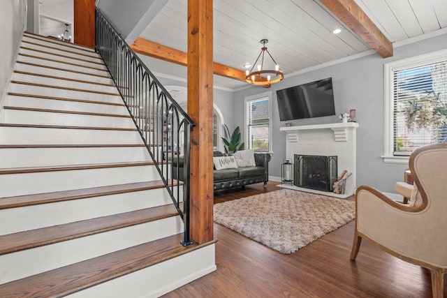 living room featuring wood finished floors, beamed ceiling, a brick fireplace, stairs, and a notable chandelier