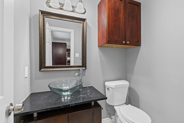 bathroom with a textured wall, vanity, and toilet