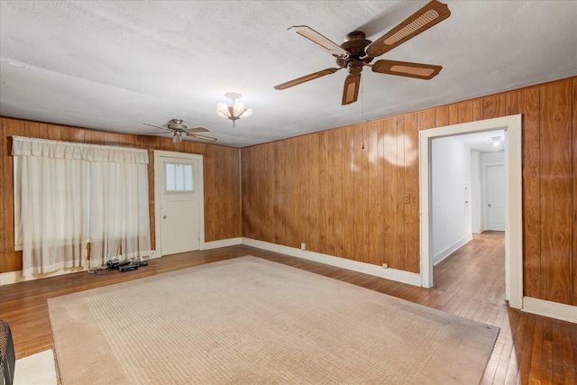 1302 E 1st St, Mount Pleasant, TX 75455 - empty room with hardwood / wood-style floors, wooden walls, a ceiling fan, baseboards, and a textured ceiling