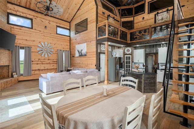 dining space featuring light wood-style flooring, wood walls, and high vaulted ceiling