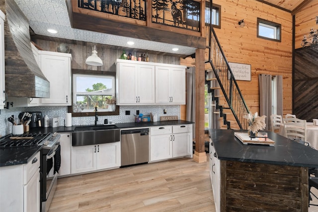 kitchen with a sink, decorative backsplash, light wood-type flooring, stainless steel appliances, and wood walls