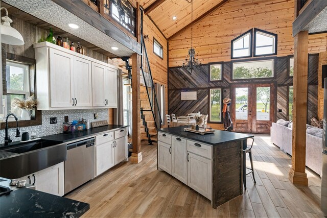 kitchen featuring high vaulted ceiling, dark countertops, dishwasher, a wealth of natural light, and wood walls