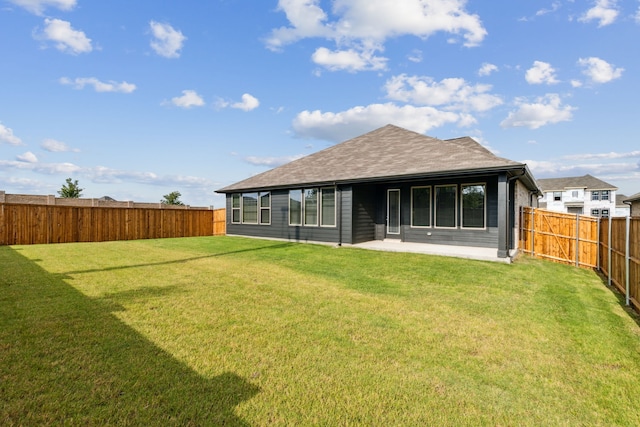 rear view of property featuring a lawn, a fenced backyard, roof with shingles, and a patio area