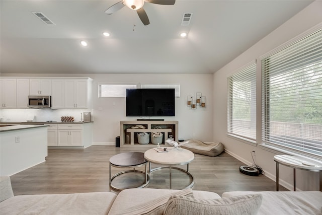 living room with lofted ceiling, a ceiling fan, visible vents, and light wood-type flooring