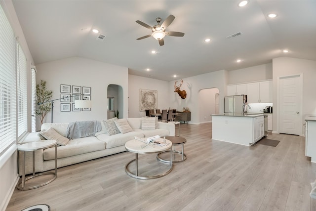 living area with light wood finished floors, arched walkways, vaulted ceiling, visible vents, and a ceiling fan
