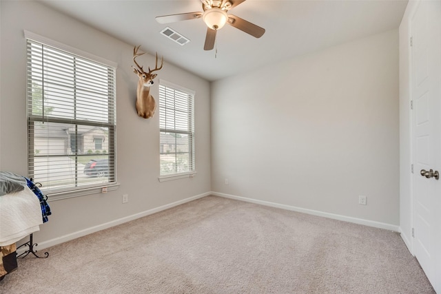 carpeted spare room featuring baseboards, visible vents, and ceiling fan