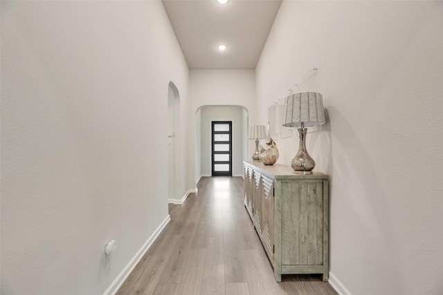 doorway to outside with baseboards, arched walkways, and light wood-type flooring