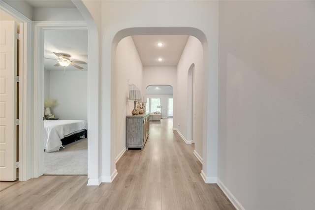 hall with arched walkways, light wood-style flooring, baseboards, and recessed lighting
