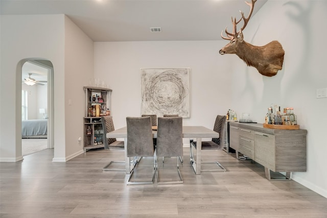 dining area with visible vents, a ceiling fan, arched walkways, light wood-type flooring, and baseboards