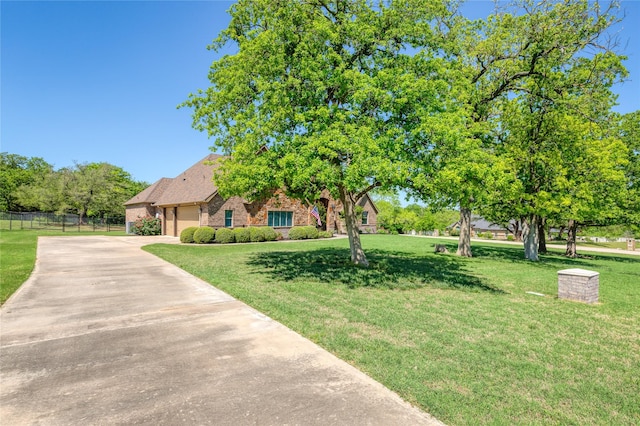 view of property hidden behind natural elements with fence, a front lawn, brick siding, and concrete driveway