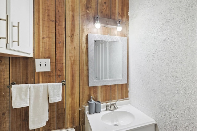 bathroom with wooden walls, a textured wall, and vanity