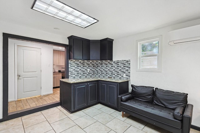 kitchen featuring a wall unit AC, dark cabinets, decorative backsplash, light stone countertops, and light tile patterned floors