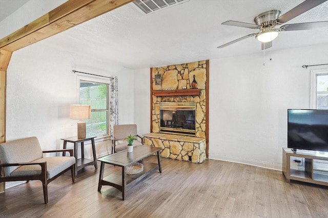 living area featuring plenty of natural light, visible vents, a stone fireplace, and wood finished floors