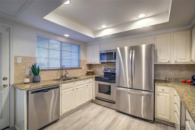 kitchen featuring backsplash, a raised ceiling, a sink, light wood-style floors, and appliances with stainless steel finishes