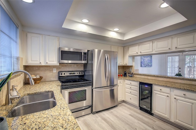 kitchen featuring a sink, decorative backsplash, stainless steel appliances, a raised ceiling, and wine cooler