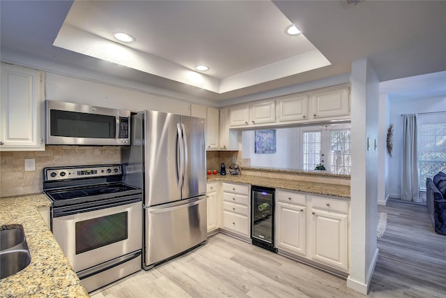 kitchen featuring wine cooler, a tray ceiling, white cabinetry, backsplash, and appliances with stainless steel finishes
