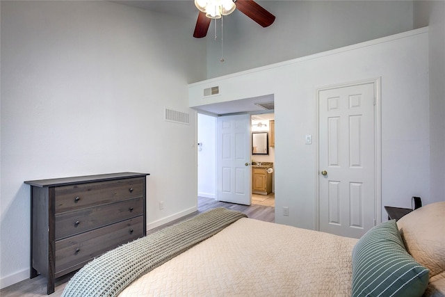 bedroom featuring light wood finished floors, baseboards, visible vents, and a towering ceiling