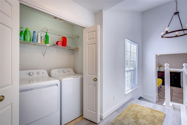 clothes washing area featuring laundry area, light wood-type flooring, baseboards, separate washer and dryer, and a chandelier