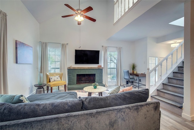 living room with light wood-type flooring, high vaulted ceiling, a ceiling fan, stairway, and a fireplace