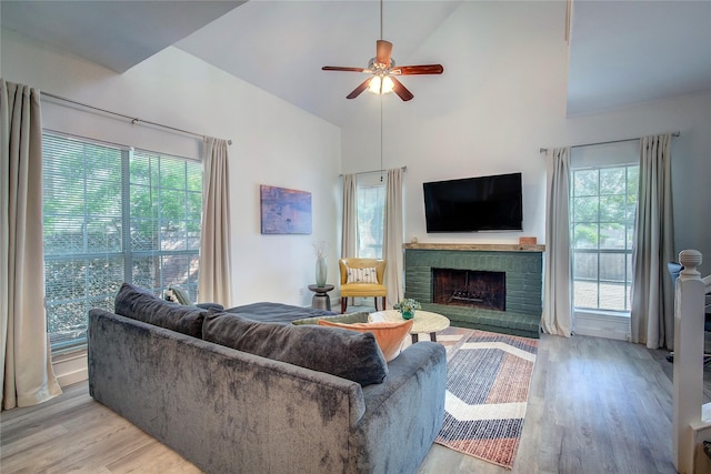 living room with a fireplace, light wood-type flooring, a wealth of natural light, and a ceiling fan