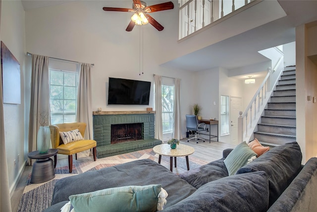 living room featuring a high ceiling, wood finished floors, stairway, ceiling fan, and a fireplace