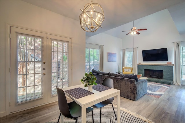dining area with high vaulted ceiling, ceiling fan with notable chandelier, wood finished floors, and a fireplace