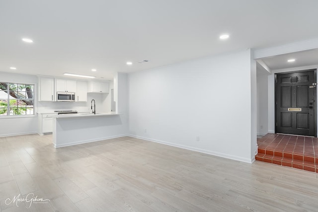 unfurnished living room with recessed lighting, light wood-type flooring, baseboards, and a sink