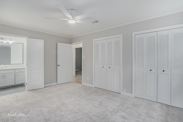 unfurnished bedroom featuring ensuite bathroom, visible vents, two closets, carpet floors, and ornamental molding