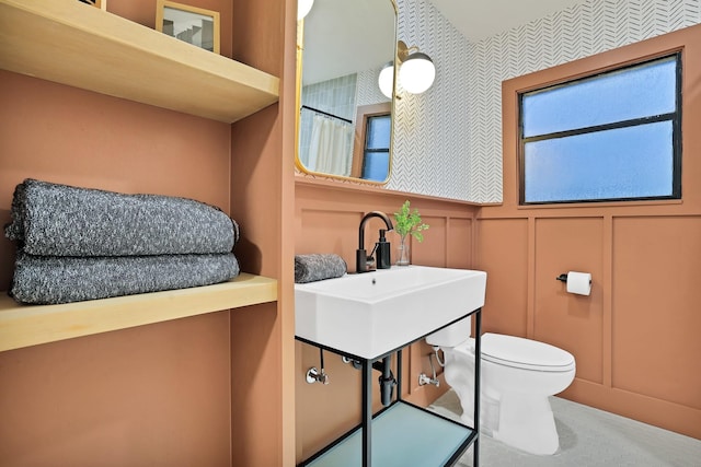 bathroom featuring toilet, a shower with curtain, a sink, and a decorative wall