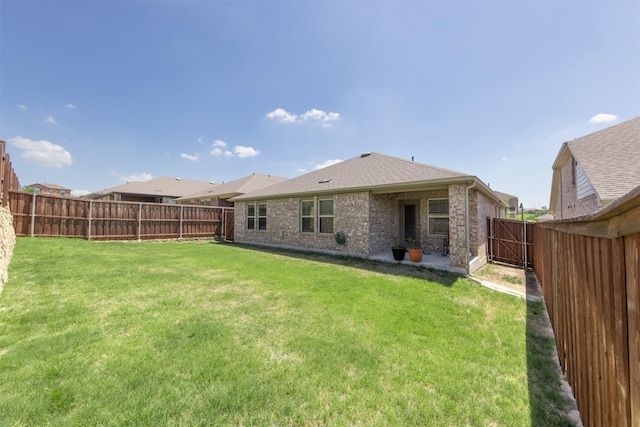 rear view of house with a shingled roof, a fenced backyard, brick siding, and a yard