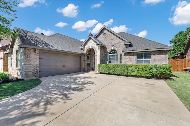 french country inspired facade with fence, concrete driveway, brick siding, and a garage
